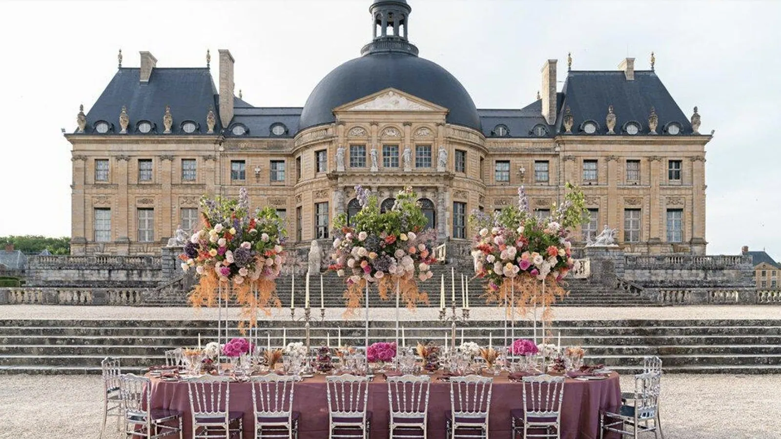 Long dinner table with tall floral arrangements set in front of a grand French château