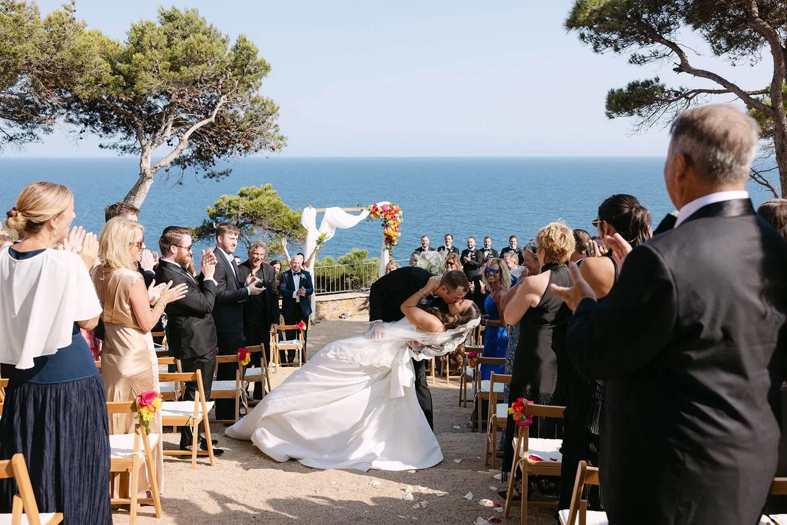 Mackenzie and Spencer share a kiss down the aisle as guests applaud at their ceremony at El Convent Blanes on the Costa Brava, Spain